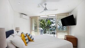 A hotel room with a bed, a ceiling fan, a TV mounted on the wall, and a view of the outdoors through large windows. - Kareka - Little Cove Serenity with Pool (Little Cove)