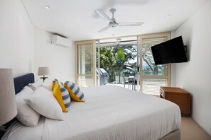 A hotel room with a bed, a ceiling fan, a TV mounted on the wall, and a view of the outdoors through large windows. - Kareka - Little Cove Serenity with Pool (Little Cove)
