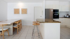 Une cuisine moderne avec un coin bar, des meubles blancs et un sol carrelé.