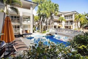 A hotel pool area with lounge chairs, a small pool, and surrounding greenery.