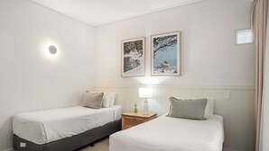 A hotel room with two single beds, a nightstand with a lamp, and two framed pictures on the wall. - Laguna 117 - Poolside, Near Beach (Noosa Heads)
