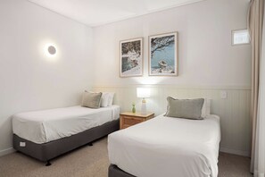 A hotel room with two single beds, a nightstand with a lamp, and two framed pictures on the wall.