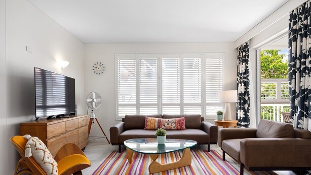 A living room with a TV, sofa, coffee table, and a striped rug. - Laguna 136 - Resort-Style, Steps to Beach (Noosa Heads)