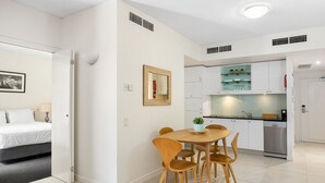 A modern hotel room with a bed, bedside table, lamp, and a dining area with a table and chairs. - Laguna 136 - Resort-Style, Steps to Beach (Noosa Heads)