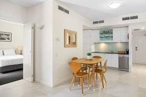 Una habitación de hotel moderna con cama, mesita de noche, lámpara y un área de comedor con mesa y sillas.