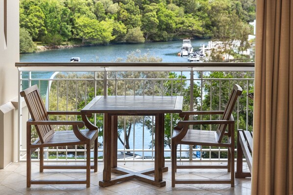 A balcony with a table and two chairs, overlooking a lake with boats and greenery.