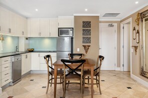 A modern kitchen with white cabinets, a stainless steel refrigerator, and a dining table with four chairs.