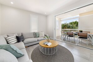 Ein modernes Wohnzimmer mit einem grauen Sofa, einem runden Couchtisch und Blick auf eine Terrasse mit Essbereich.