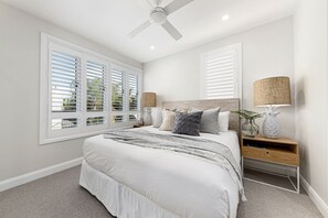 A bedroom with a bed, bedside tables, a ceiling fan, and windows with blinds.