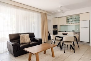 Un salon moderne avec un canapé en cuir noir, une table basse en bois et un coin repas comprenant des chaises blanches et une table avec un plateau en verre.
