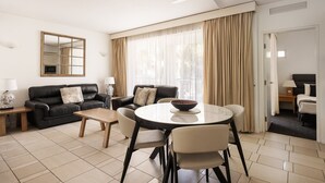 A modern living room with a sofa set, a dining table with chairs, a ceiling fan, and a large window with curtains. - Laguna 621 - Oasis on Hastings St (Noosa Heads)
