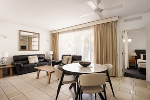 Ein modernes Wohnzimmer mit einer Sofagarnitur, einem Esstisch mit Stühlen, einem Deckenventilator und einem großen Fenster mit Vorhängen.