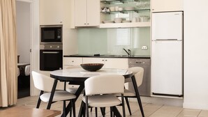 A compact kitchen with white cabinets, a black countertop, a glass-top dining table, and a white refrigerator. - Laguna 621 - Oasis on Hastings St (Noosa Heads)