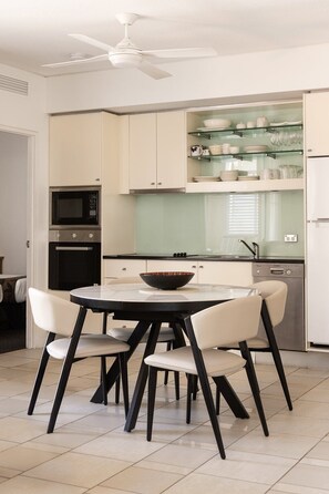 A modern kitchen with a round dining table, four chairs, a ceiling fan, and built-in appliances. - Laguna 621 - Oasis on Hastings St (Noosa Heads)