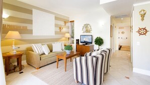 Ein Wohnzimmer mit einer Couch, Sesseln, einem Couchtisch, einem Fernseher, Wanddekoration und einem Schiffsrad.