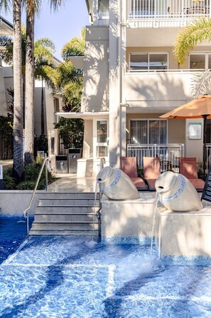 A pool area with a hot tub, steps leading to the pool, and a building with balconies. - Laguna 622 - Nautical Romance in Noosa (Noosa Heads)