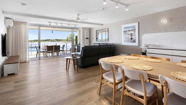 A modern living room with a dining area, large windows, and a view of the sea. - Las Rias, Riverside Luxury Bliss (Noosa Heads)