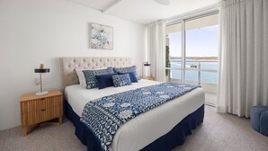A bedroom with a large bed, a ceiling fan, a nightstand, a lamp, and a view of the water. - Las Rias, Riverside Luxury Bliss (Noosa Heads)