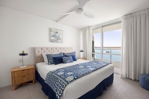 A bedroom with a large bed, a ceiling fan, a nightstand, a lamp, and a view of the water. - Las Rias, Riverside Luxury Bliss (Noosa Heads)