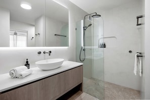 Features a sleek vessel sink, large mirror, and glass-enclosed walk-in shower with handheld showerhead.