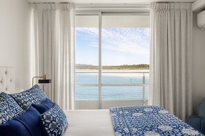 A room with a bed, a sofa, and a view of a beach and water.