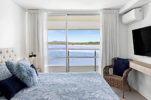 Relax in this serene retreat with a large bed, sliding glass door to a balcony overlooking a body of water, and a flat-screen TV.
