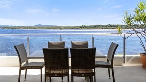 A terrace with wicker chairs and a table overlooking a beach and water.