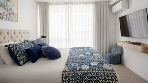 A modern bedroom with a large bed, a TV, and a window with curtains.