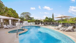 A swimming pool with lounge chairs and umbrellas, surrounded by palm trees and a clear sky. - Las Rias, Riverside Luxury Bliss (Noosa Heads)