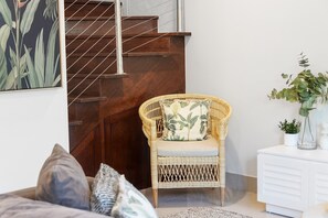 Une chaise en osier avec un coussin, une armoire blanche, un escalier et un tableau encadré au mur.
