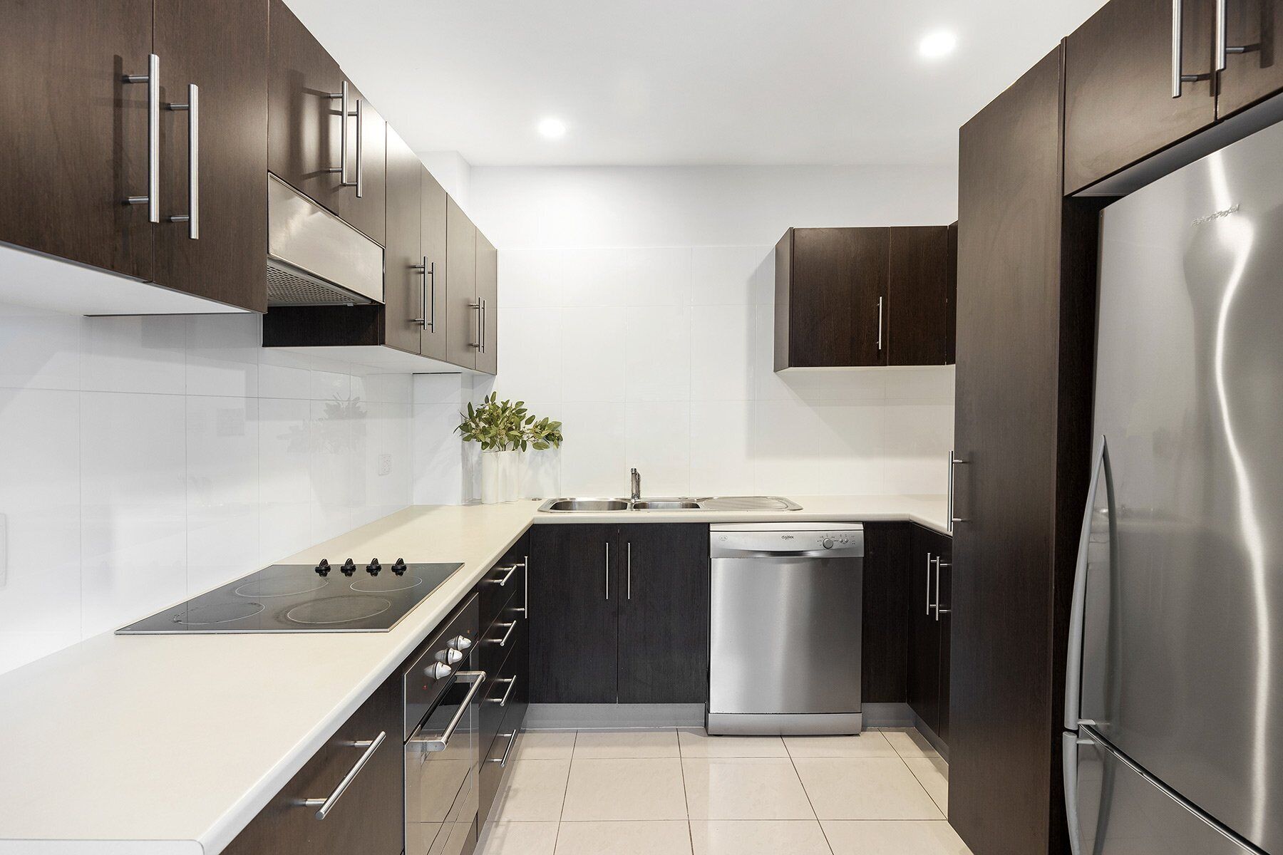 Una cocina moderna con armarios oscuros, electrodomésticos de acero inoxidable y encimera blanca.