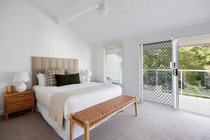Une chambre avec un grand lit, un banc en bois, une table de chevet et une vue sur un balcon extérieur, accessible par une porte-fenêtre coulissante.