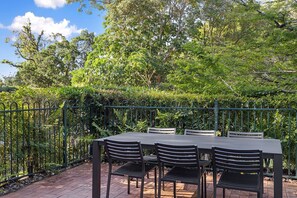 Un patio al aire libre con una mesa y sillas, rodeado por una cerca de metal verde y follaje exuberante.