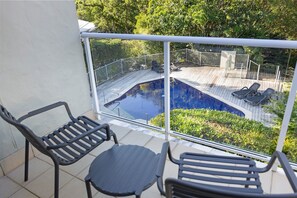 A balcony with a view of a swimming pool, two lounge chairs, and a small table.