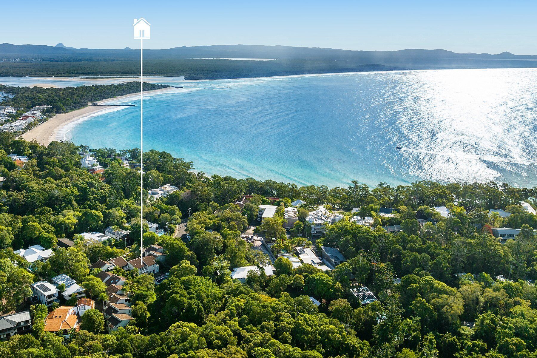 Vista aérea de una zona costera con playa, abundante vegetación y cielo despejado.