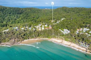 Vista aérea de una zona costera con playa, bosque denso y edificios dispersos.