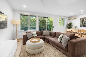 A modern living room with a sectional sofa, a round ottoman, and a dining area with a table and chairs.
