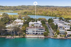 A coastal residential area with a prominent multi-story building featuring balconies, a dock, and a clear view of the surrounding water and hills.