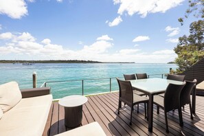 A deck with a table and chairs, overlooking a body of water with boats and a distant shoreline.
