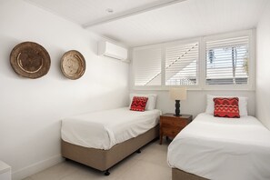 A bedroom with two beds, a nightstand, a lamp, and a wall-mounted air conditioner.