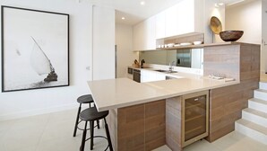 Een moderne keuken met een centraal eiland, barkrukken, een ingebouwde oven en een groot raam.