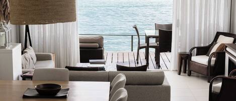 A modern living room with a view of the sea, featuring a sofa, dining table, and chairs.