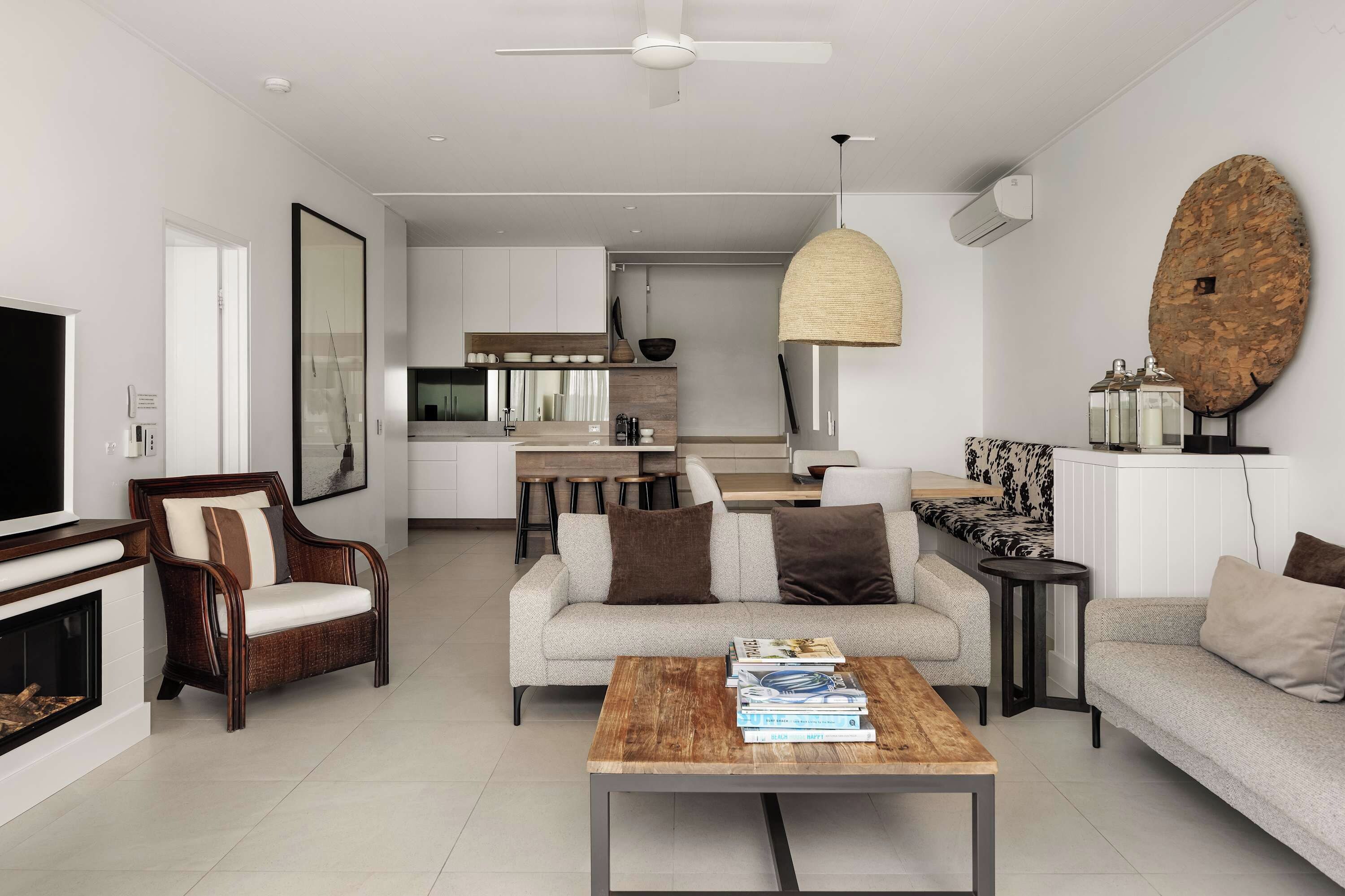 A modern living room with a fireplace, a sofa, a coffee table with books, and a kitchen in the background.