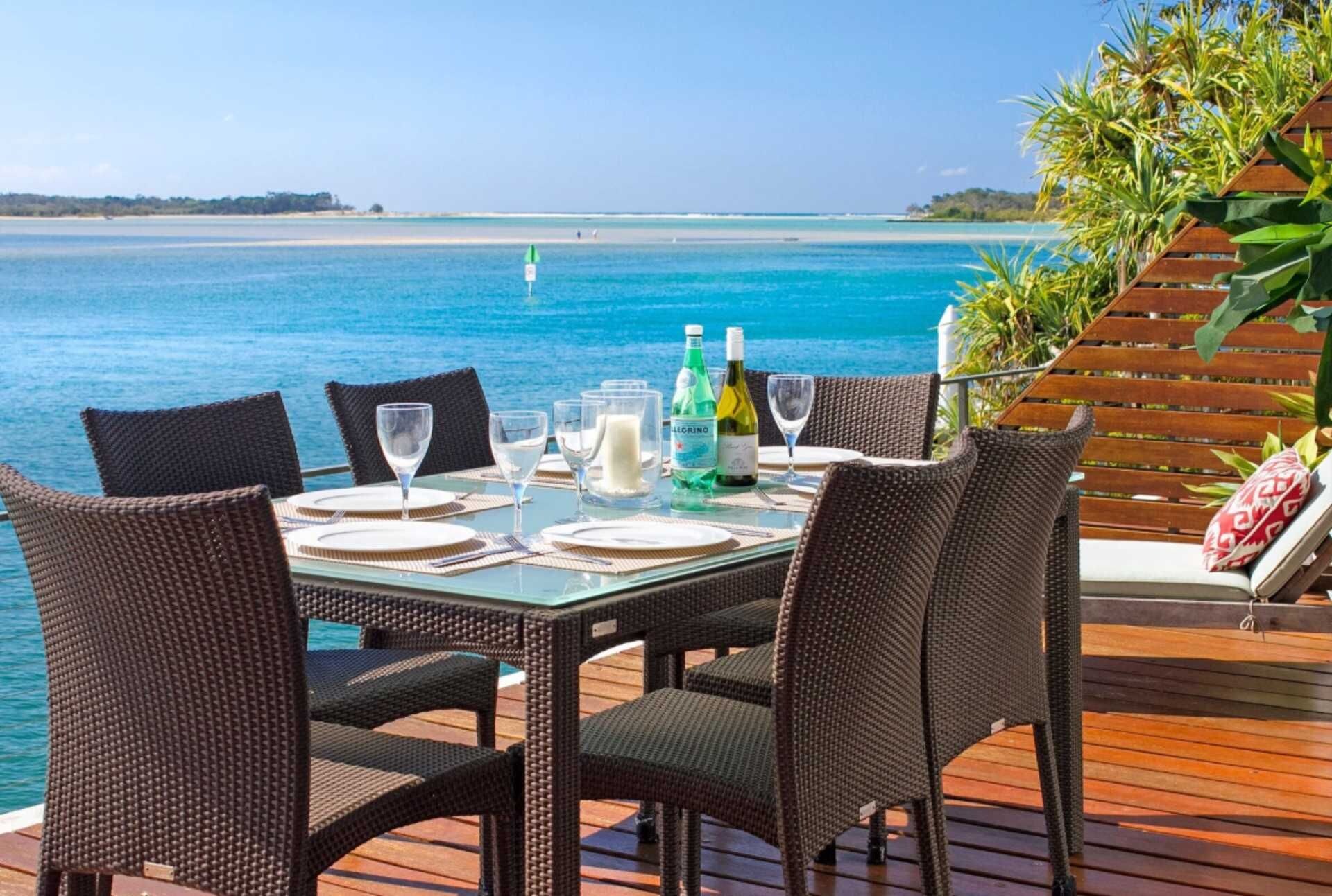 Mesa de comedor para seis personas con sillas, vista al mar y terraza de madera.