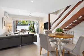 Relax in this stylish living room with a sofa, dining table, and TV, plus a balcony with a view of lush surroundings.