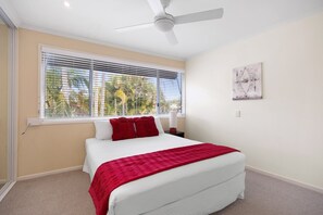 Ein Schlafzimmer mit Bett, Deckenventilator, Fenster mit Jalousien und einem Wandbild.