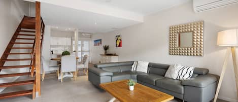 Ein modernes Wohnzimmer mit einem grauen Ecksofa, einem Holztisch und einer Treppe.