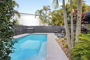 Relax in a serene outdoor oasis with a pool surrounded by lush greenery and comfortable seating areas.