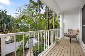 Ein Balkon mit Korbstuhl, weißer Reling und tropischen Pflanzen.