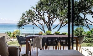 An outdoor dining area with a view of the sea, surrounded by greenery and a large tree.